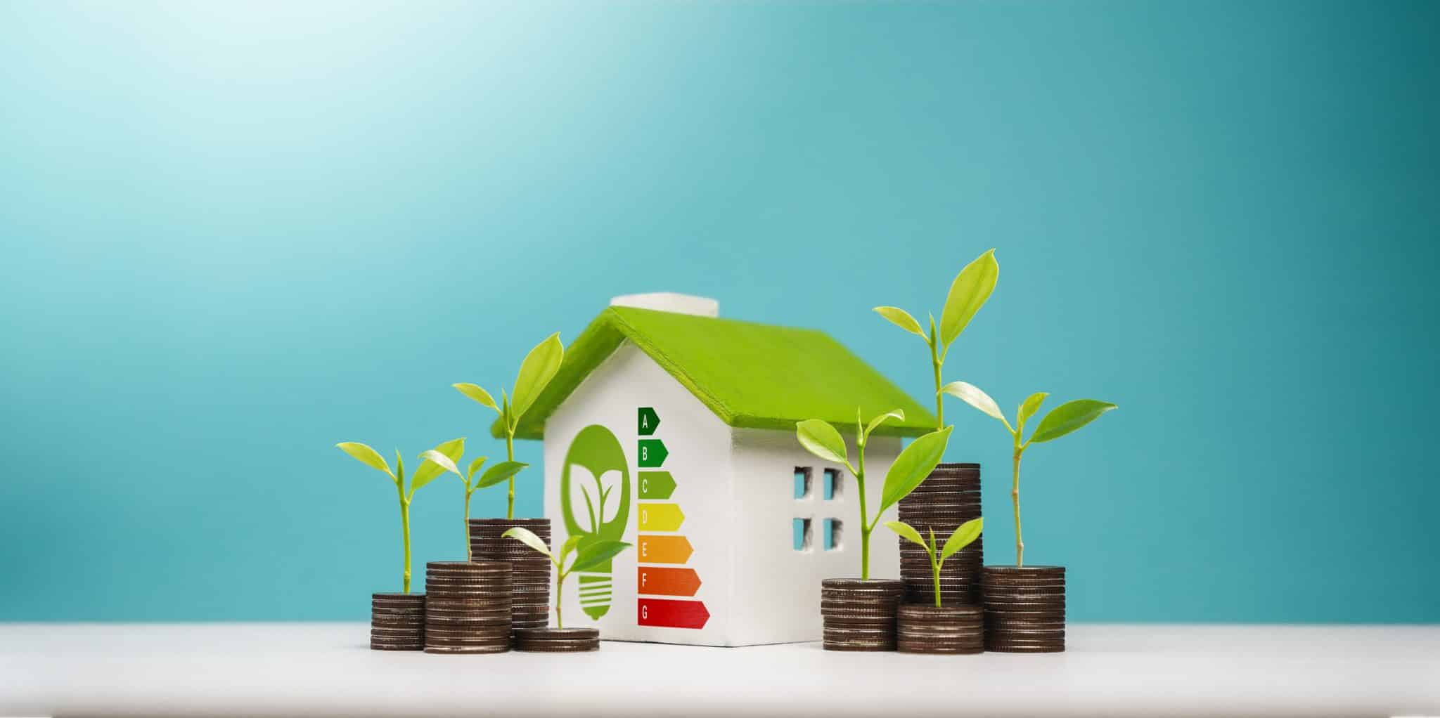 A miniature house with an energy efficiency rating chart surrounded by stacked coins with green seedlings growing from them